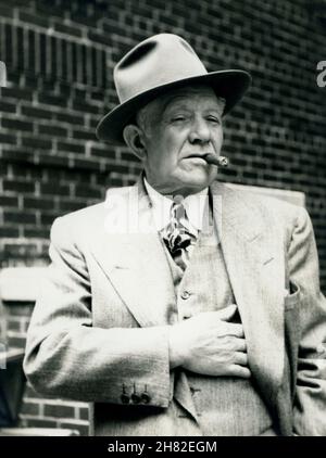 Vecchio uomo in un ambiente urbano con un sigaro, cappello e vestito fedora, circa 1950. Foto Stock