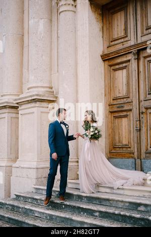 Sposa e sposo si trovano sui gradini di pietra dell'antica chiesa alla porta Foto Stock
