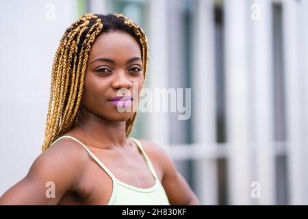 Primo piano ritratto di una giovane donna africana di bellezza con capelli intrecciati di fronte alla macchina fotografica all'aperto Foto Stock
