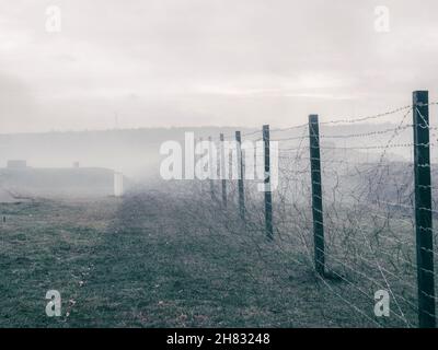 Righe di filo spinato sul confine dello stato. La separazione dei due paesi. Nebbia paesaggio autunnale Foto Stock