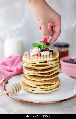 ragazza decora mette bacche su frittelle con banana e bacche Foto Stock