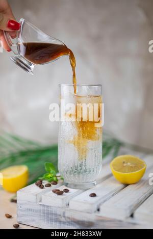 ragazza il barman versa il caffè espresso con limone nel tonico Foto Stock