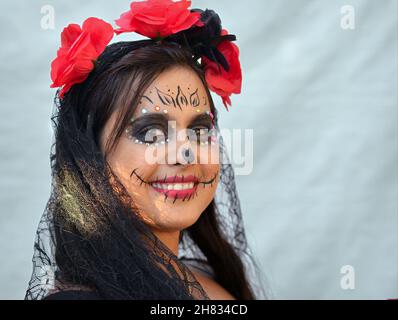 Allegro positivo ottimista giovane messicana Yucatecan donna con tradizionale Catrina viso trucco e glitter viso gioielli sorride il giorno dei morti. Foto Stock