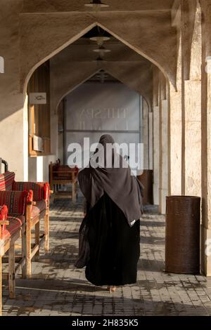 Vecchio mercato in Souq Waqif - bazaar orientale in Doha. Una signora araba che cammina nella vista posteriore del souq Foto Stock