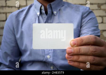 Uomo d'affari che consegna un biglietto da visita vuoto su sfondo bianco muro di mattoni sulla strada. Una carta di credito di plastica o carta da visita come mockup per i desi Foto Stock