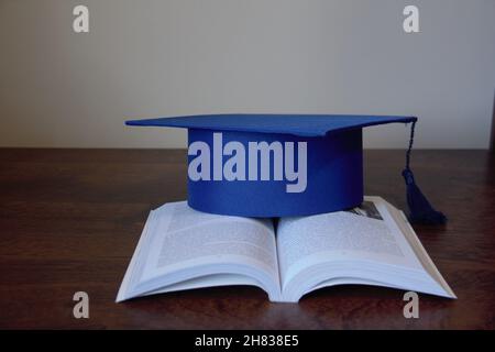 Tappo graduato, isolato, su un libro aperto su un tavolo di legno con sfondo bianco. Foto Stock