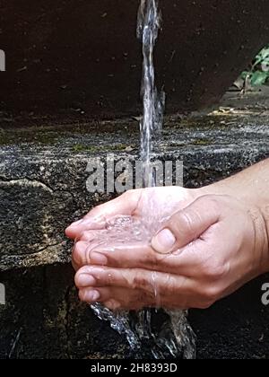 Mani maschili che tengono l'acqua in un beccuccio naturale in un parco. Foto Stock