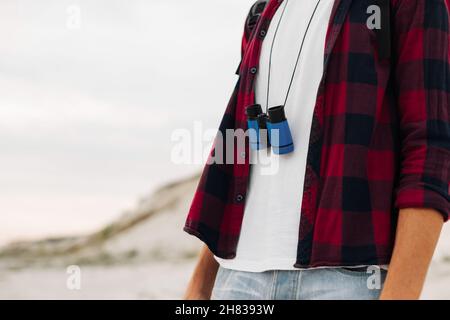 Viaggiatore maschile con uno zaino che guarda attraverso binocoli all'aperto nella natura. Il ragazzo guarda attraverso binocoli sulla collina. Un uomo con binocolo e un Foto Stock