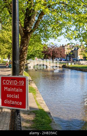 Un segno sociale di allontanamento accanto al fiume Windrush nel villaggio Cotswold di Bourton sull'acqua, Gloucestershire Regno Unito durante l'epidemia di Covid 19. Foto Stock