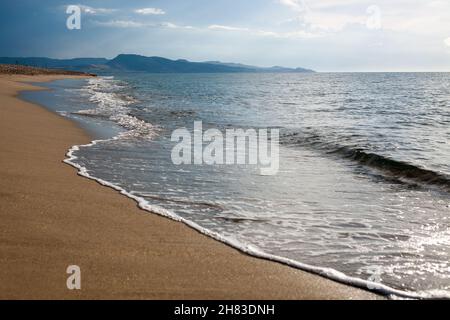 Inquadratura ad angolo basso della spiaggia sabbiosa, con impronte e alghe, lambite da onde in rapido movimento. Foto Stock