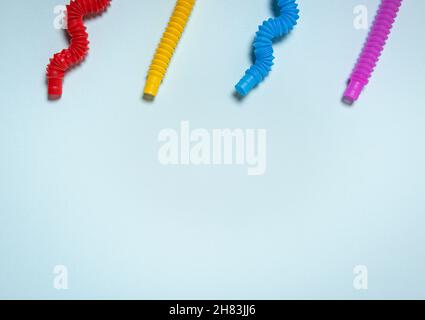 Dritto e piegato a forma d'onda colorato giallo brillante, rosso, rosa e blu pop tubo giocattoli per bambini. Quattro giocattoli antistress in plastica a contrasto su pa blu Foto Stock
