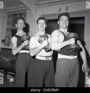 1965, storico, all'interno di una stanza, tre membri della squadra di sollevamento pesi del servizio civile degli uomini posano per una foto nel loro corredo che tiene i dumbbells, Fife, Scozia, Regno Unito. Foto Stock