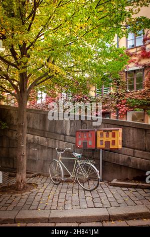 Una bicicletta bianca è parcheggiata sul lato della strada vicino ad alcune scatole a forma di casa posta nei vicoli posteriori di Stoccolma Svezia Foto Stock