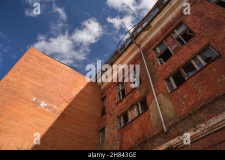 Abbandonata fabbrica sovietica in mattoni rossi con finestre rotte e downpipe con cielo blu Foto Stock