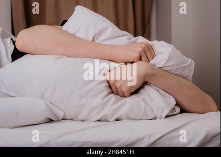L'uomo depresso giaceva da solo a letto coprendo la testa con un cuscino, impaurito o depresso, affetto da insonnia, vicini forti, dopo un divorzio da h Foto Stock