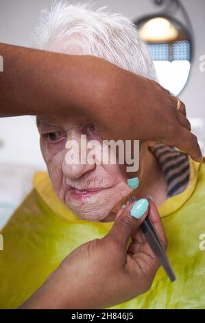 donna anziana che riceve la rimozione dei capelli del viso da un operatore sanitario afroamericano Foto Stock