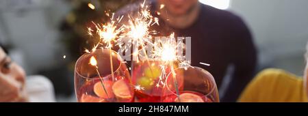 Gruppo di persone che bevono cocktail da bicchieri con scintille di fronte al primo piano albero di natale Foto Stock