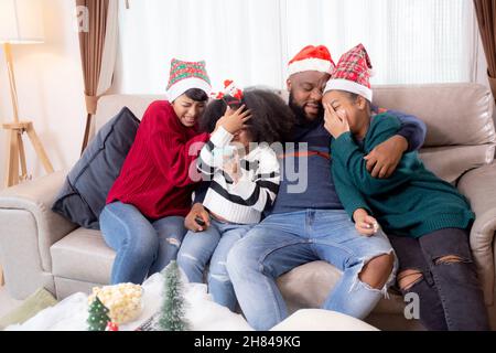 Happy famiglia africana seduta sul divano guardando la TV con film horror nel soggiorno di casa, genitori e bambini guardare la televisione con paura uno Foto Stock