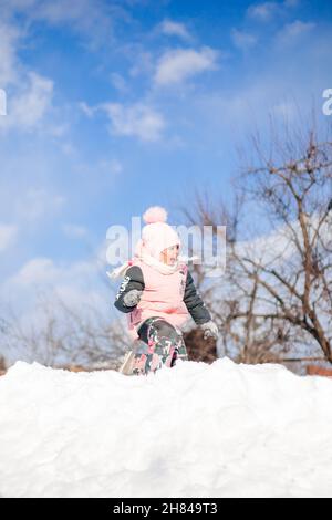 Scivoli per bambini. Bambina in inverno vestito caldo gioca in aria fresca e gode giorno di sole in inverno, lei si trova nella neve e gioca palle di neve Foto Stock