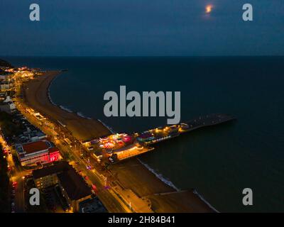 Una fotografia aerea di Hastings, Sussex, UK, Inghilterra, scattata in un'ora blu con il molo illuminato e che si aggetta in mare. Foto Stock