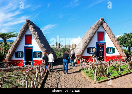 I turisti che visitano le famose case di Santana, le tradizionali case triangolari, tipiche dell'isola di Madeira, in Portogallo, in Europa. Foto Stock