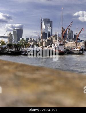 Una vista della città di Londra scattata dalla riva nord del tamigi in una giornata nuvolosa con nuvole fluide, barche a raschietto e cieli grigi. Foto Stock