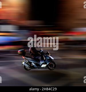 Un colpo di panning di una persona che guida un ciclomotore con le luci di Piccadilly Circus sullo sfondo. Londra. Foto Stock