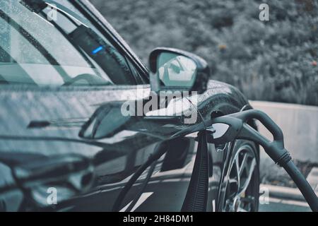 Vista laterale di un'auto moderna nera lucida che riempie il benzene con uno sfondo di alberi sfocati Foto Stock
