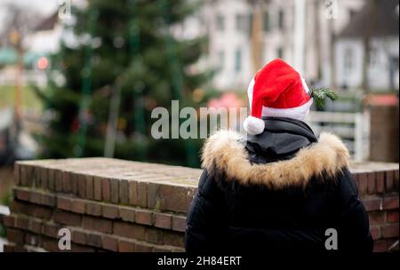 Carolinensiel, Germania. 27 novembre 2021. Una donna in un cappello di Natale guarda l'albero galleggiante di Natale che è messo in su nel porto della città. Dal 1995, l'albero è stato tradizionalmente messo in su e le luci accese il Sabato prima della prima Domenica in Avvento. Credit: Hauke-Christian Dittrich/dpa/Alamy Live News Foto Stock