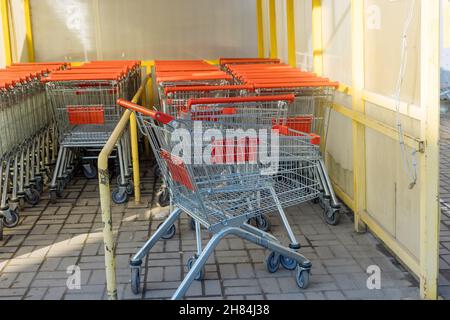 Una fila di carrelli metallici vicino ad un centro commerciale sono collocati in una fila in un ipermercato Foto Stock