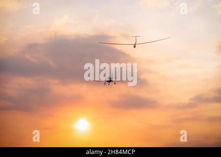 un piccolo aereo motore che tira un aliante nel sole che tramonta Foto Stock