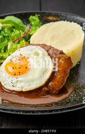 Primo piano di una cotoletta di manzo con uova fritte, purè di patate e insalata fresca su un piatto Foto Stock