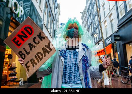 Amsterdam, Paesi Bassi. 27 novembre 2021. Un attivista XR che indossa abiti di seconda mano tiene una targhetta contro il Black Friday durante la dimostrazione.Extinction Rebellion ha organizzato nel centro di Amsterdam una sfilata di moda, per dare un'aria alla moda veloce e per attirare l'attenzione sulle pratiche di sfruttamento, profitto e lavaggio del verde del settore della moda veloce. Gli attivisti del clima marciarono attraverso le principali strade dello shopping danzando e indossando abiti riparati e di seconda mano. (Foto di Ana Fernandez/SOPA Images/Sipa USA) Credit: Sipa USA/Alamy Live News Foto Stock