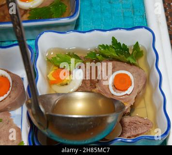 Jelly brodo viene colata dalla siviera cucchiaio in stampo con ingredienti della lingua in bellavista piatto che sono disponendo in ceramica rettangolare piatti di insalata. Foto Stock