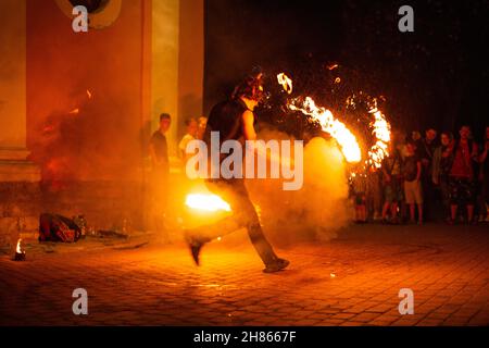 Un ragazzo fa uno spettacolo di fuoco sulla strada di notte intorno ad una folla di persone Foto Stock