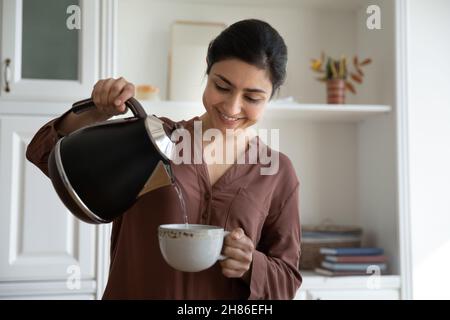 Sorridente giovane etnia indiana donna versando acqua calda in tazza. Foto Stock