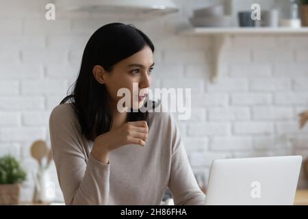 Giovane donna asiatica premurosa seduta al coperto con un computer portatile Foto Stock