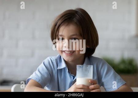 Il ragazzo bello con i baffi del latte tiene un bicchiere di latticini Foto Stock