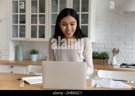 La donna asiatica guarda il laptop sorridendo leggere le notizie delle merci Foto Stock