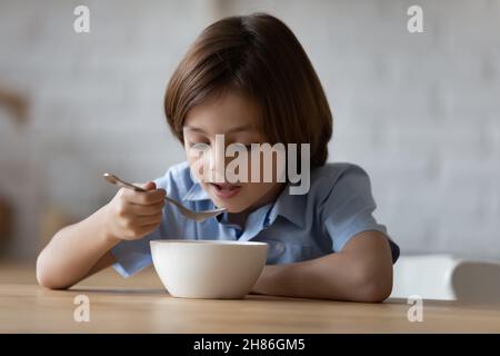 Il ragazzino si siede in cucina tiene il cucchiaio mangiare porridge Foto Stock