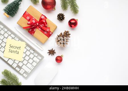 Vista dall'alto foto di giftbox con adesivo di prua rosso nota carta su tastiera computer mouse penna rosso albero di natale palle di abete giocattolo pino rametti coni e anice o Foto Stock