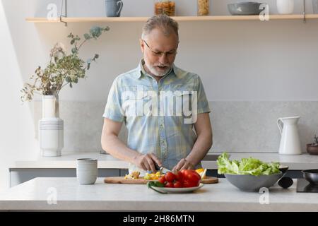 Senior grigio capelli vegetariano uomo cottura pranzo in cucina Foto Stock