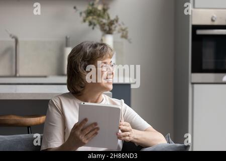 Signora felice pensierosa matura seduta sul divano in buoni pensieri Foto Stock