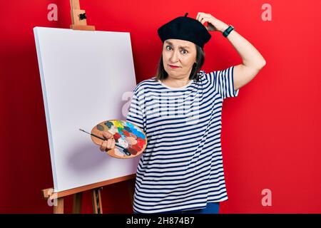 Medievale donna ispanica in piedi disegno con tavolozza dal pittore cavalletto stand confusi e domandandosi circa domanda. Incerto con dubbio, pensando wi Foto Stock