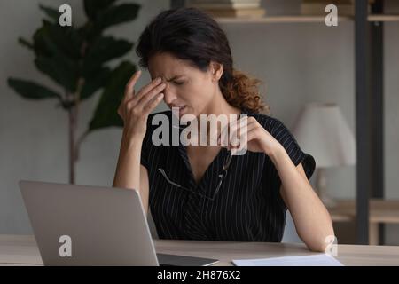 Stanco dipendente latino donna ufficio strofinare naso togliere occhiali Foto Stock