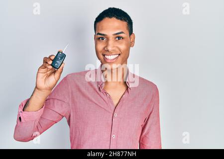 Giovane africano americano che tiene la chiave della nuova vettura sembrando positivo e felice in piedi e sorridendo con un sorriso sicuro che mostra i denti Foto Stock