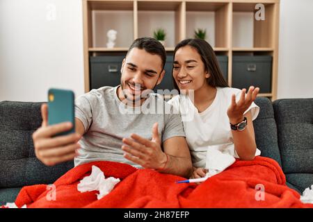 Giovane coppia malata latina che ha teleconsulto medico utilizzando smartphone a casa. Foto Stock