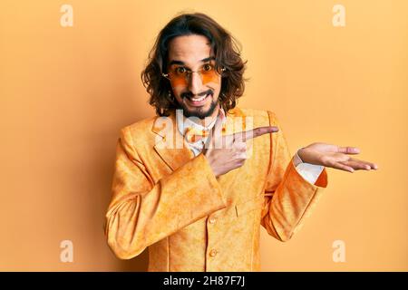 Giovane uomo ispanico che indossa l'hipster elegante look stupito e sorridente alla fotocamera mentre si presenta con la mano e punta con le dita. Foto Stock