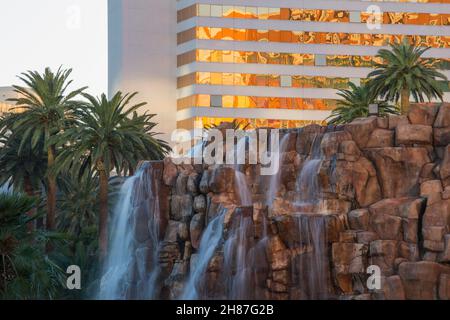 Las Vegas, Nevada, Stati Uniti. Cascata ornamentale che cade su scogliere di roccia rossa al di fuori del Mirage Resort and Casino, tramonto, palme sullo sfondo. Foto Stock