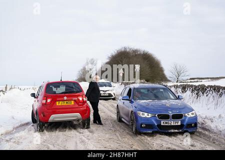 I veicoli tentano di viaggiare lungo la A515 innevata nei pressi di Biggin, nel Peak District, Derbyshire, in mezzo a condizioni di gelo all'indomani di Storm Arwen. Data foto: Domenica 28 novembre 2021. Foto Stock